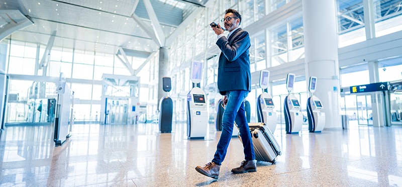 Man walking through an airport rolling luggage and talking on a cellphone
